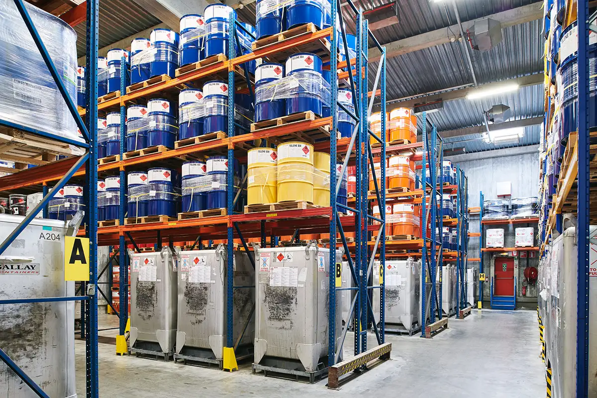 Entrepôt avec des barils bleus, jaunes et oranges empilés sur des étagères métalliques, illustrant le stockage chez Dandoy Warehousing.