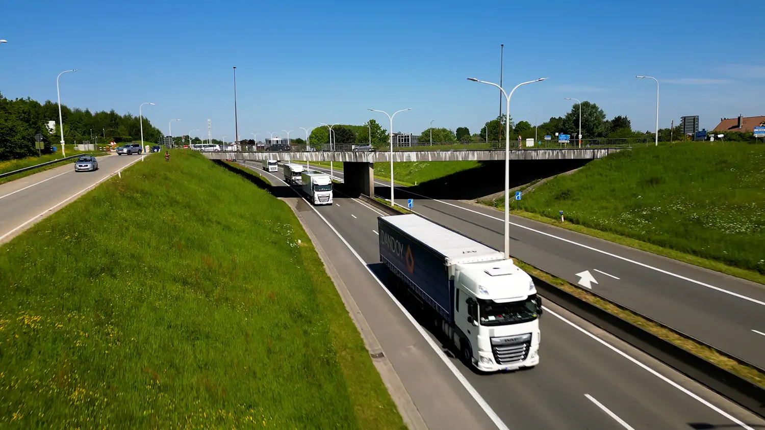 Camion blanc Dandoy circulant sur une autoroute entourée de verdure sous un ciel bleu dégagé.