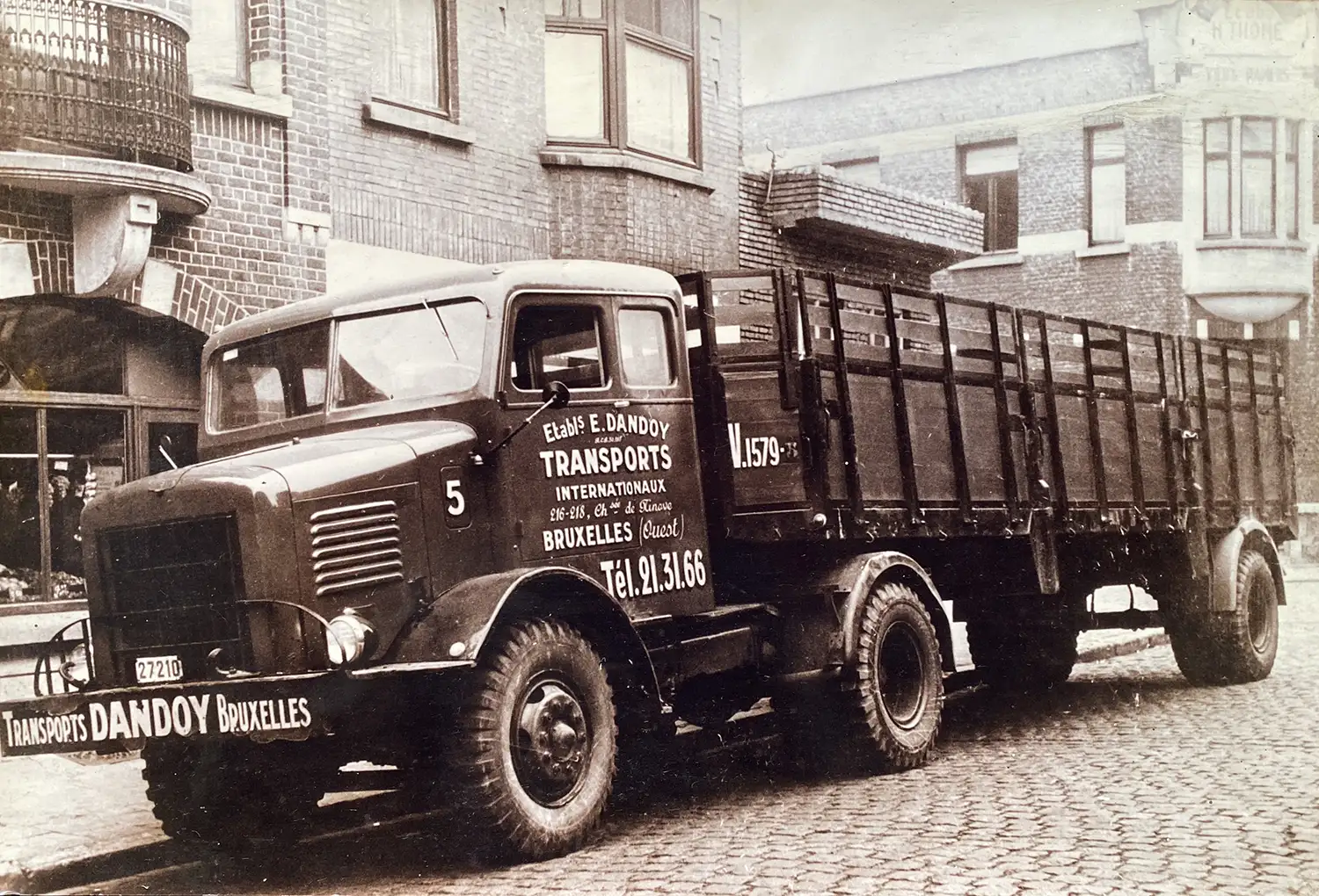 Camion ancien de transport Dandoy Bruxelles garé devant un bâtiment en briques, avec des inscriptions sur la carrosserie.