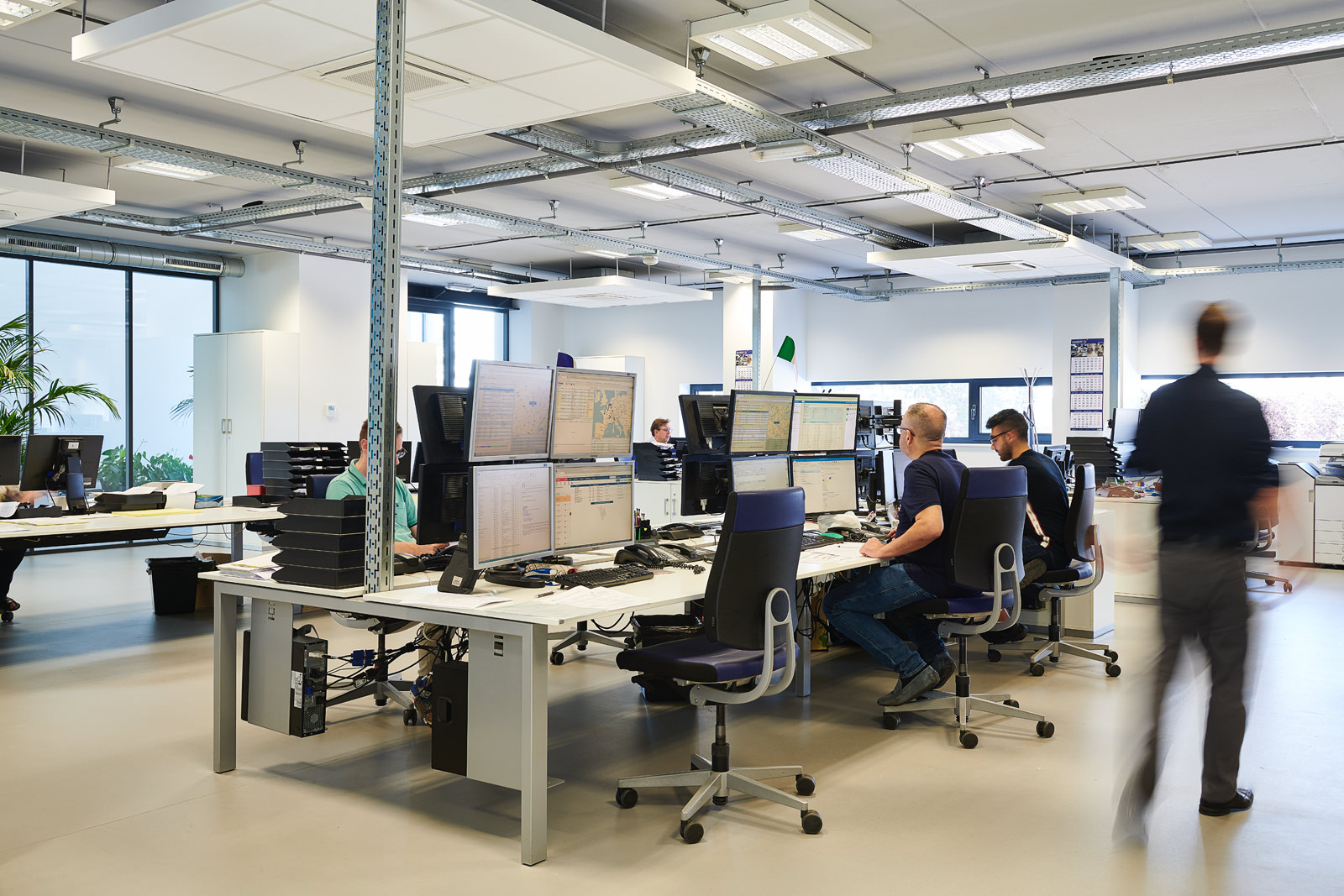 Des employés travaillent dans un bureau moderne équipé de nombreux écrans d'ordinateur sur des bureaux blancs.