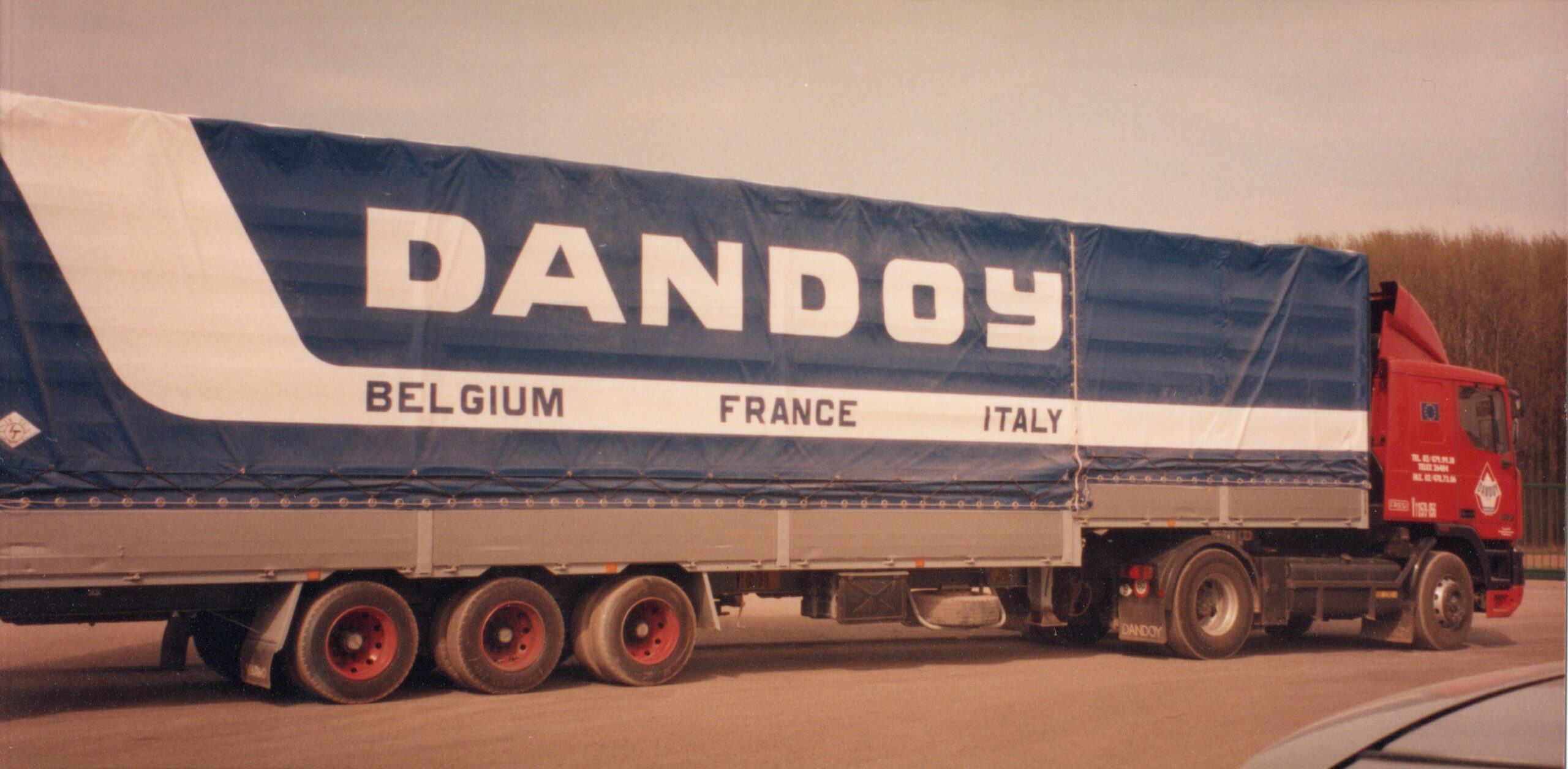 Un camion rouge avec une remorque bleue affichant "Dandoy" et "Belgium France Italy", image img20241022_11564313.